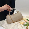A hand holds a shimmering beige envelope clutch with a gold chain strap on a white textured surface.