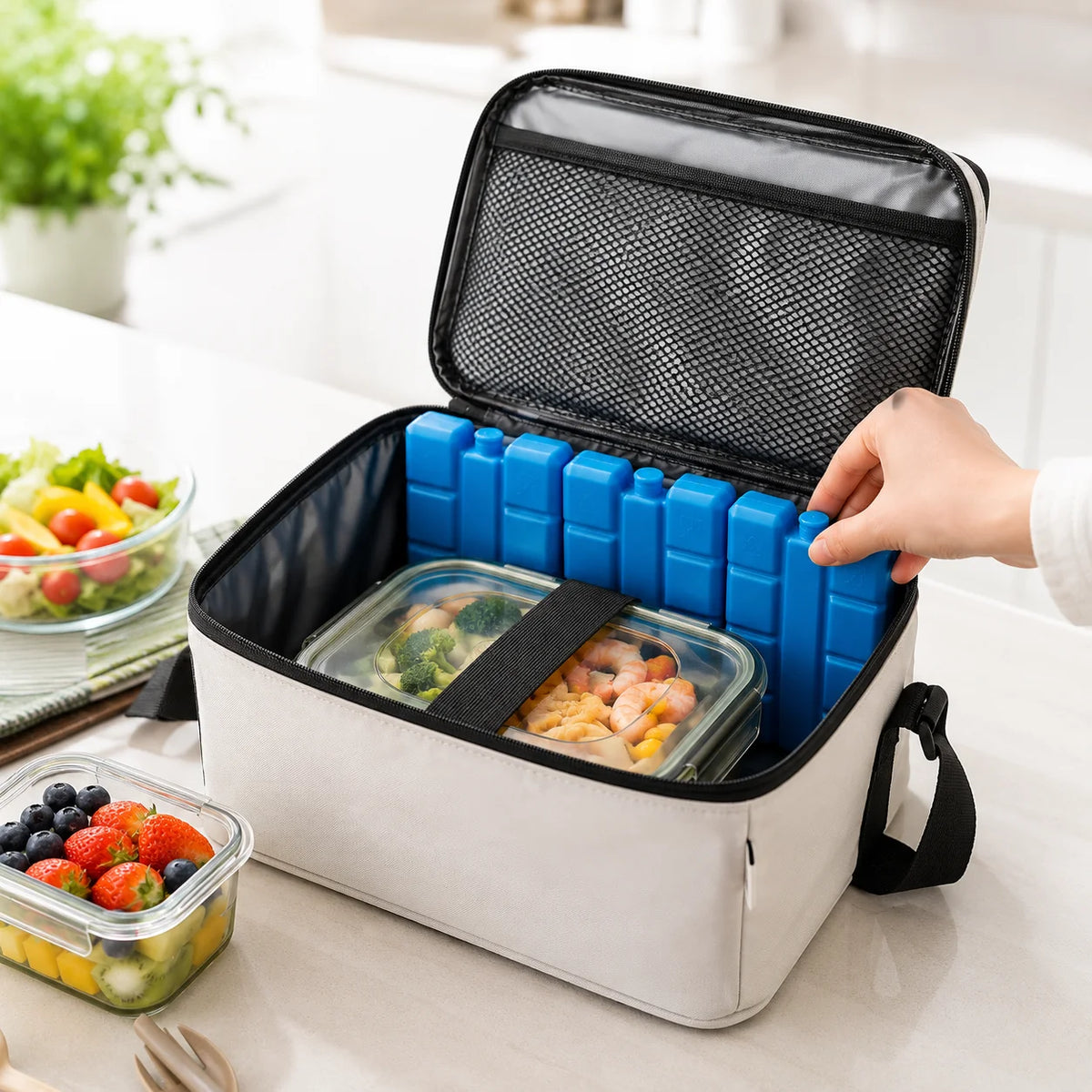 A white reusable cooler box with a black lid and blue gel ice blocks is shown open on a table.