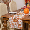 Linen table runner featuring an orange pumpkin and maple leaf pattern on a wooden table.