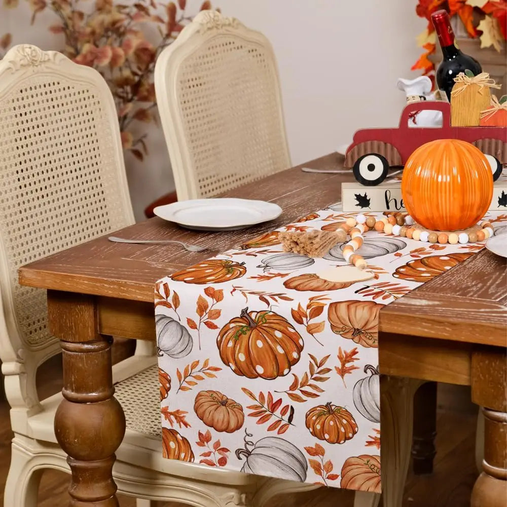 Linen table runner featuring an orange pumpkin and maple leaf pattern on a wooden table.
