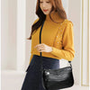 A woman wearing a mustard yellow turtleneck sweater and dark skirt holds a black compact square crossbody bag.