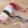 A collection of sheer satin ribbon rolls in shades of pink, red, and black laid out on a wooden surface.