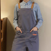 A person wearing a gray adjustable polyester kitchen apron over a light blue shirt.