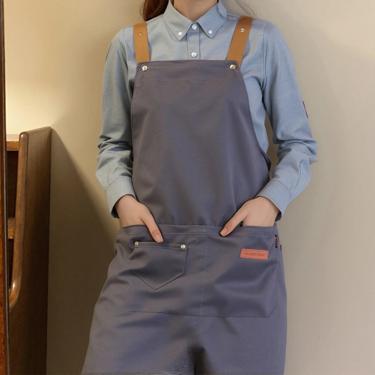 A person wearing a gray adjustable polyester kitchen apron over a light blue shirt.