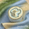 A roll of gradient cake yarn showing soft blue and beige colors displayed on a light blue fabric.