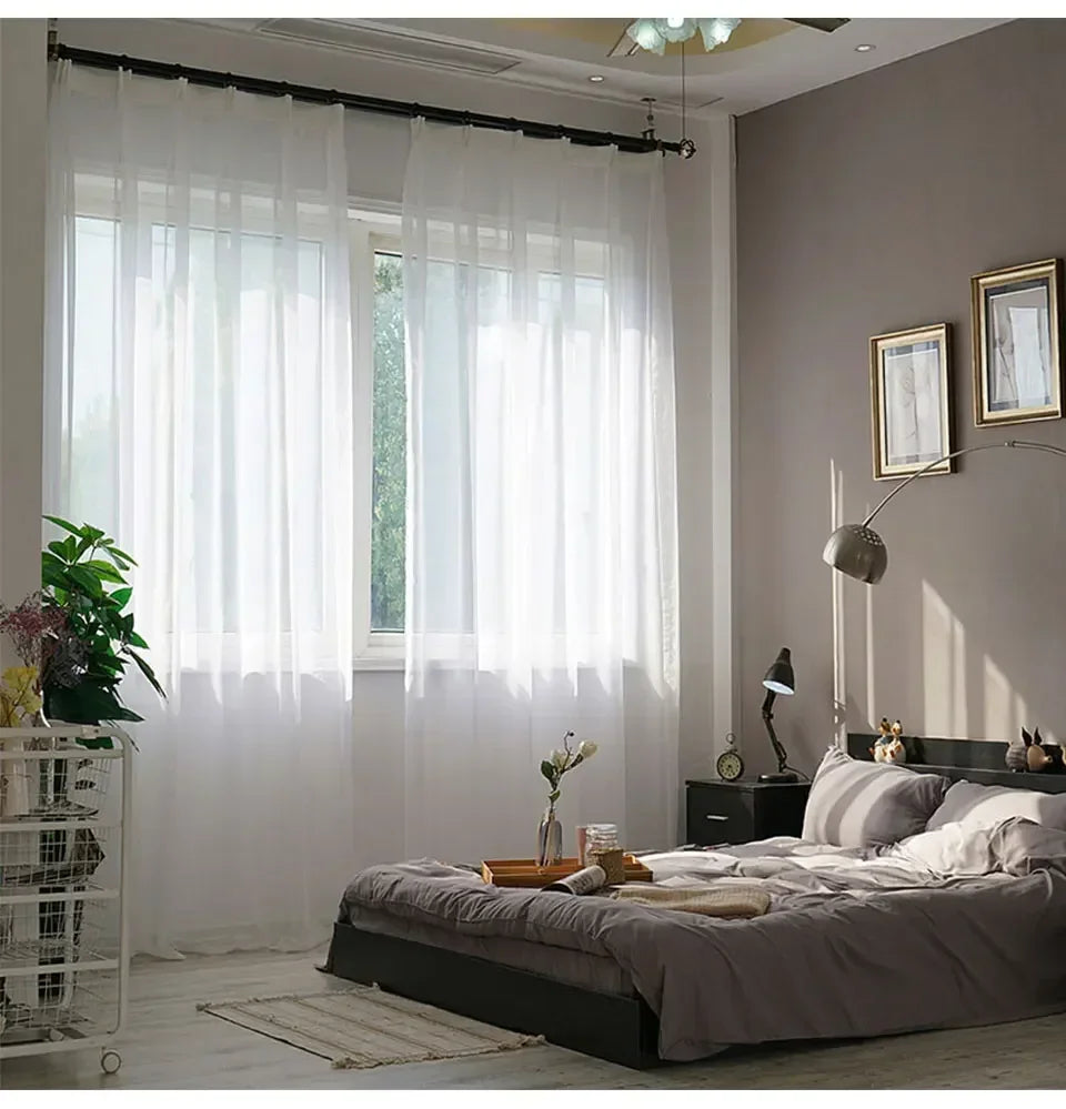 Durchscheinende weiße Tüllvorhänge, die ein Fenster in einem modernen Schlafzimmer drapieren.