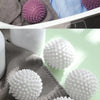 Close-up of white and pink reusable laundry balls on a gray knitted fabric.