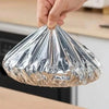 A hand is holding a reusable aluminum foil bowl cover, which is shaped like a cone.