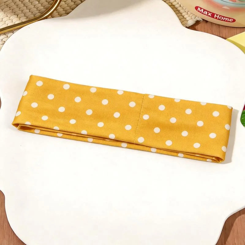 Un bandeau de tissu jaune à pois blancs posé sur une surface blanche.