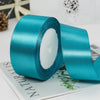 A roll of teal satin ribbon with white filler, lying on a sheet of paper.