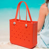 Orange tragbare EVA Strandtasche liegt auf hellem Sand mit verschwommenem blauem Wasser im Hintergrund.