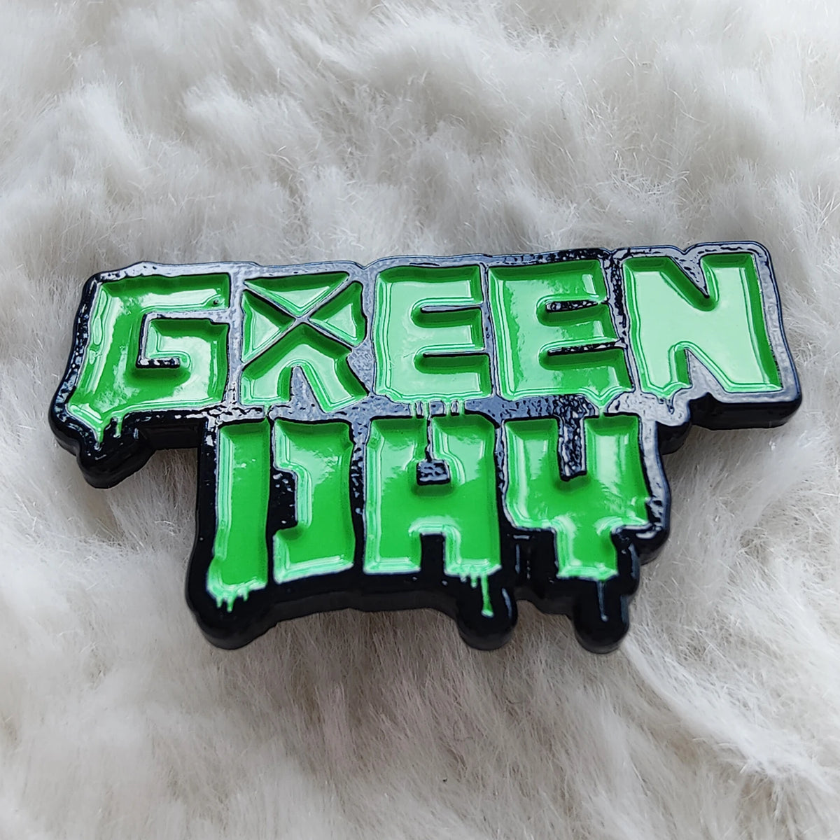 A green rock band day pop singer pin lapel brooch metal badge jewelry accessory with a distressed finish.