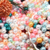 A close-up of various round imitation pearl beads in shades of pink, blue, gold, and green scattered on a white surface.