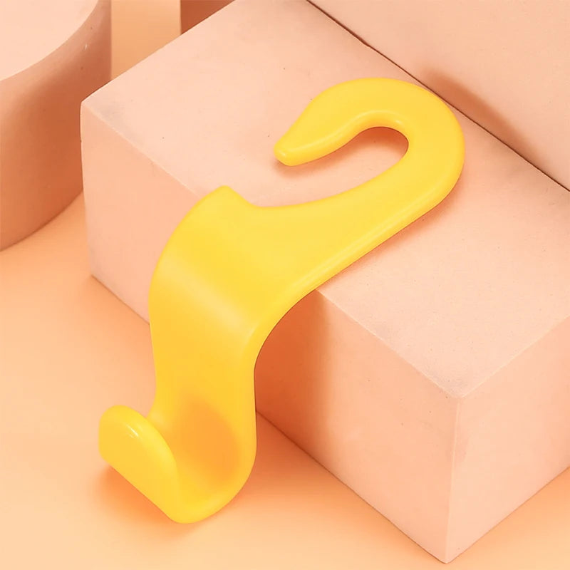 A pair of yellow universal car seat headrest hooks resting on a light pink rectangular surface.