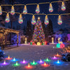 Outdoor holiday display featuring warm yellow string lights and colorful LED lights illuminating a snowy yard with a decorate