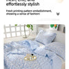 A light blue floral patterned quilted blanket is displayed on a bed, featuring a two-tone print.