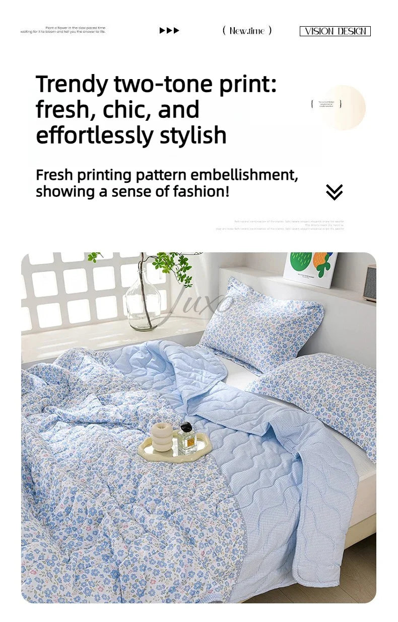 A light blue floral patterned quilted blanket is displayed on a bed, featuring a two-tone print.