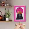 A pink framed display featuring a black candy jar with a dust cover, held by a pair of hands.