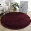 A deep burgundy shaggy round rug placed on a light wooden floor in a living room setting.