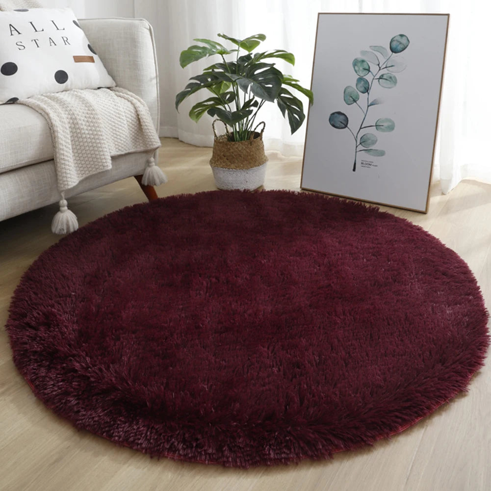 A deep burgundy shaggy round rug placed on a light wooden floor in a living room setting.
