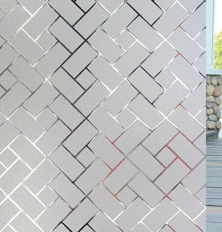 A close-up of a wall covered in light gray, textured brick tiles with a repeating herringbone pattern.