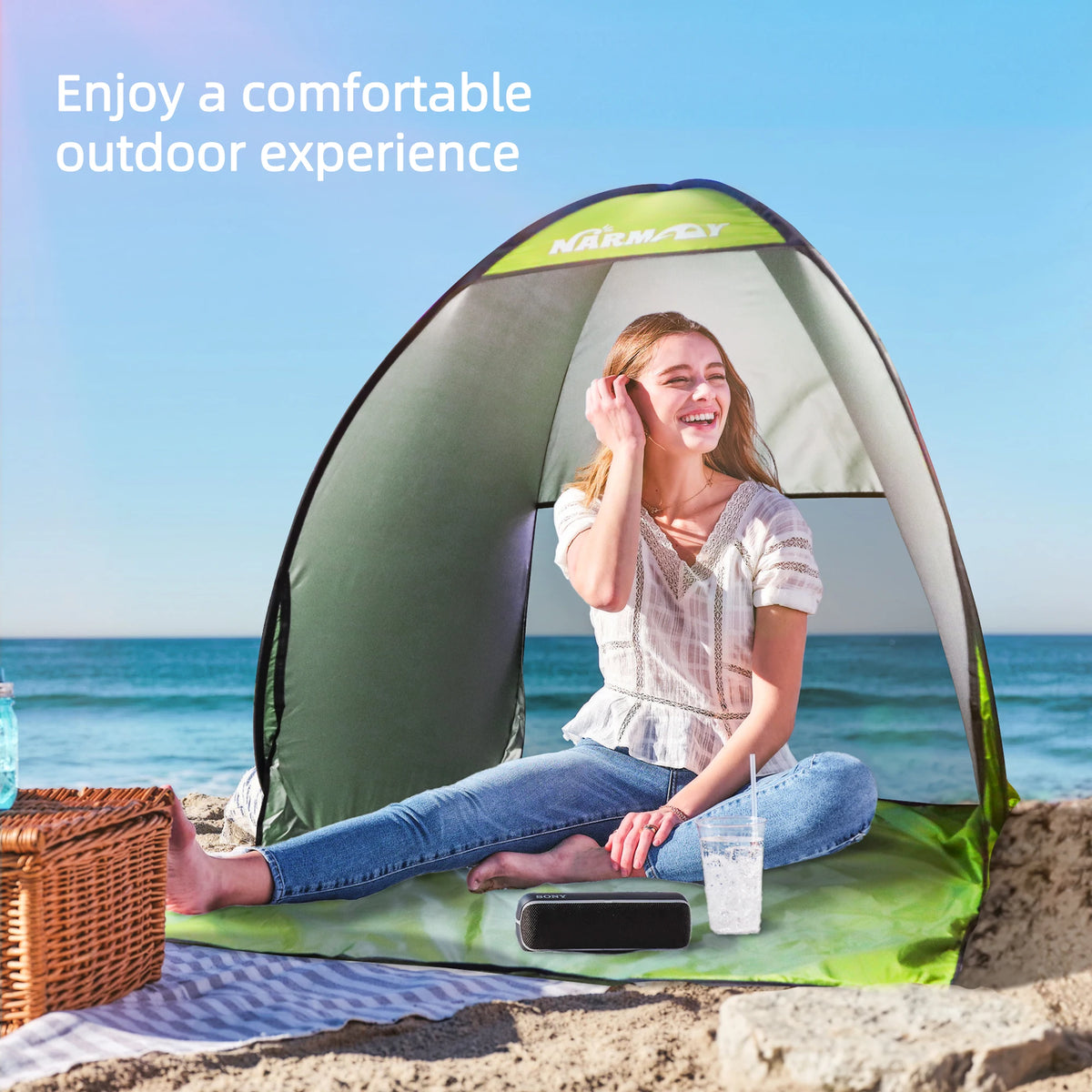 A woman smiling inside a green and gray instant pop-up beach tent enjoying an outdoor experience by the sea.