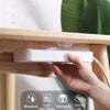 A hand is installing a white invisible adhesive hook onto a wooden surface, demonstrating its use for removable wall hooks.