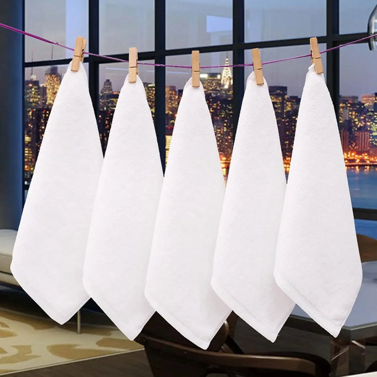Five white soft cotton terry cloth face towels are hanging on a clothesline against a cityscape background.