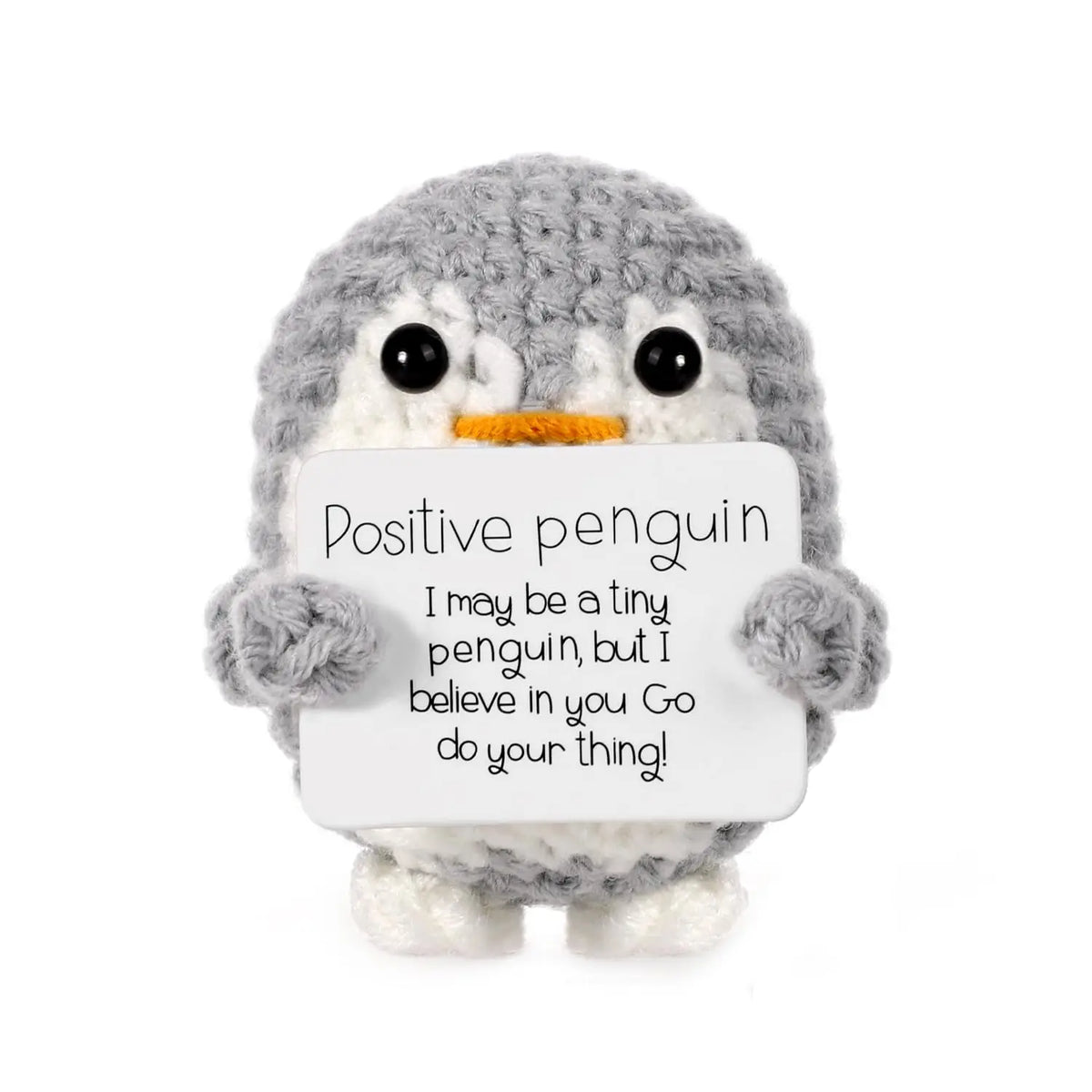 A gray crocheted penguin figurine holding a card with the text Positive penguin I may be a tiny penguin but I believe in you 