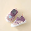 A pair of purple and pink knitted baby shoes with a textured sole resting on a light beige background.