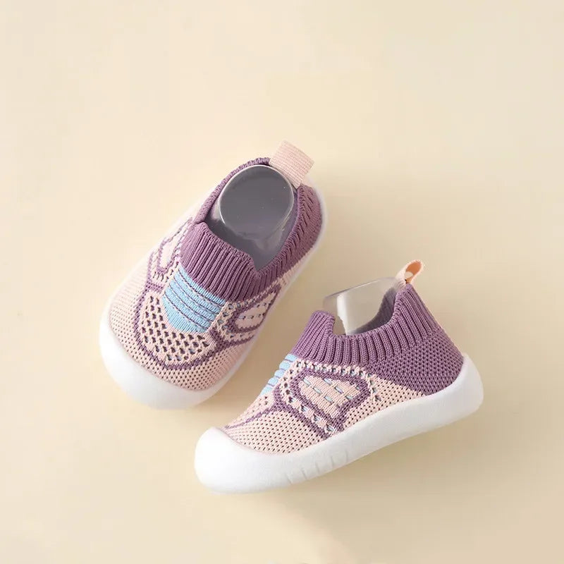 A pair of purple and pink knitted baby shoes with a textured sole resting on a light beige background.