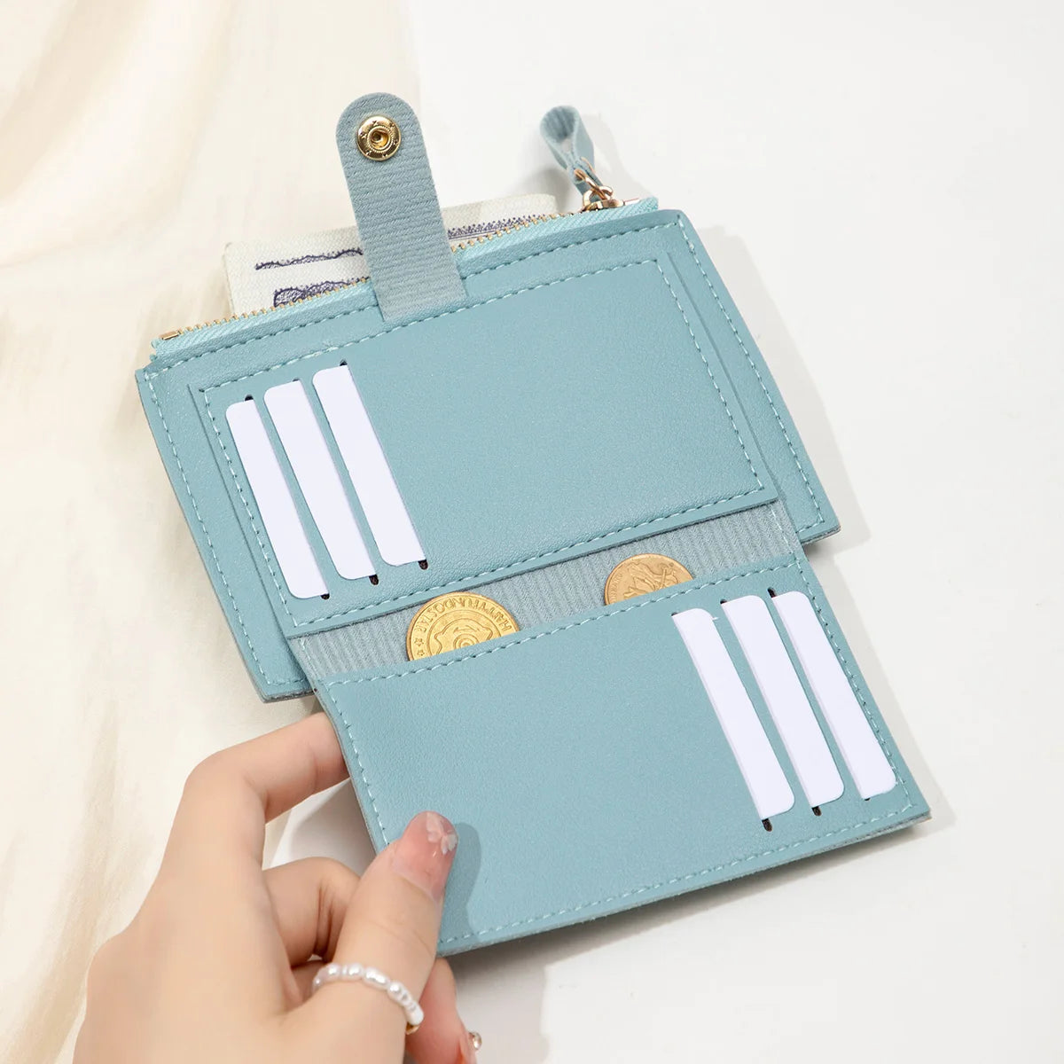 A light blue card holder wallet with a leather strap and gold accents is held by a hand.