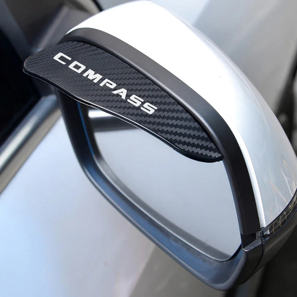 A close-up of a black compass branded rain guard visor attached to a silver Jeep Compass side mirror.