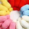 A collection of brightly colored yarn skeins in yellow, red, blue, and pink stacked on a white surface.