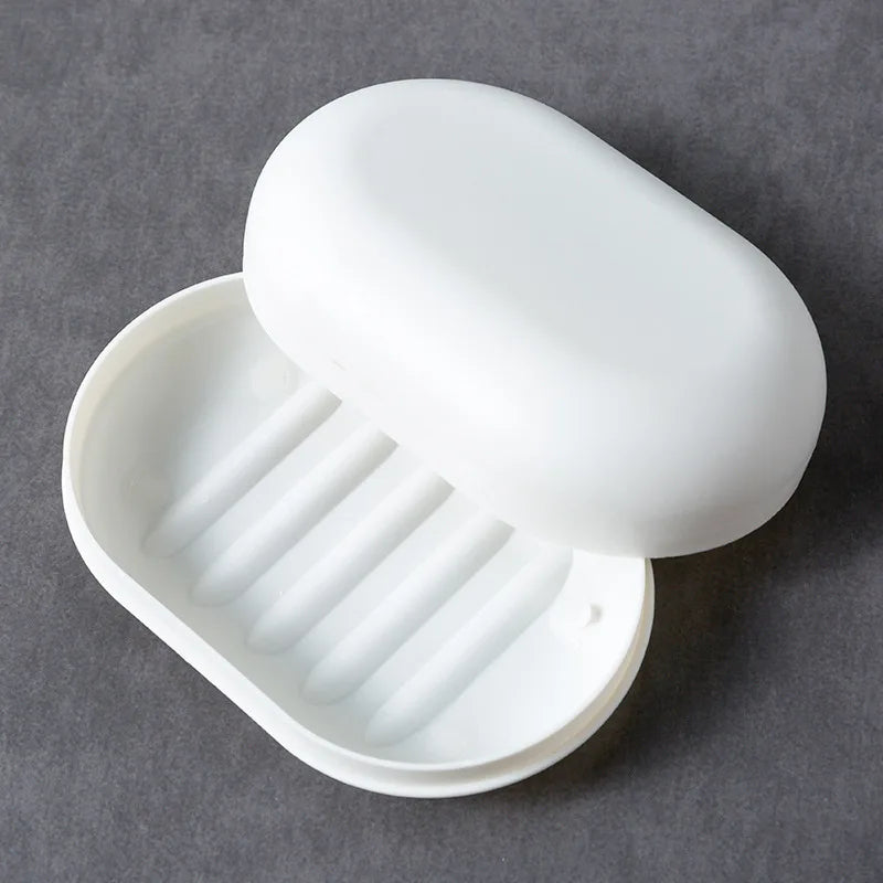 A white portable soap dish with a lid is shown open, displaying ribbed compartments for holding soap.
