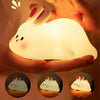 A glowing white silicone rabbit night light held in a person's hand, with three smaller versions shown below.