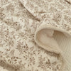 Close-up of a floral muslin baby blanket in beige with brown botanical prints, showing soft texture and folds.