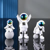 A set of three handcrafted astronaut figurines made of white resin with reflective blue helmets displayed on a glossy surface