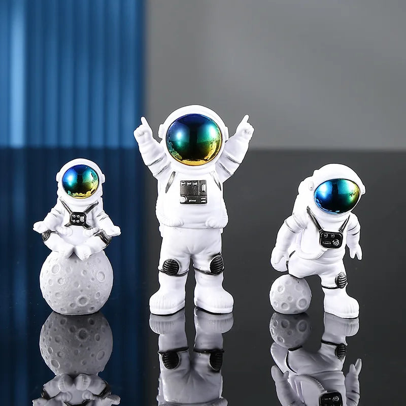 A set of three handcrafted astronaut figurines made of white resin with reflective blue helmets displayed on a glossy surface