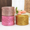 Three spools of metallic flat ribbon yarn in pink, rose gold, and gold stacked on a white surface.