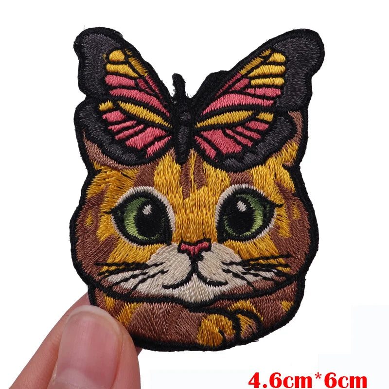 Embroidered patch of a cartoon cat butterfly with orange and black fur and pink wings