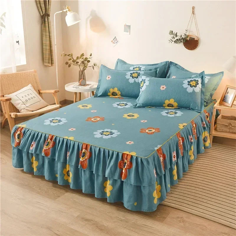 Une jupe de lit imprimée bleu sarcelle avec des motifs floraux jaunes et oranges est exposée sur un lit.