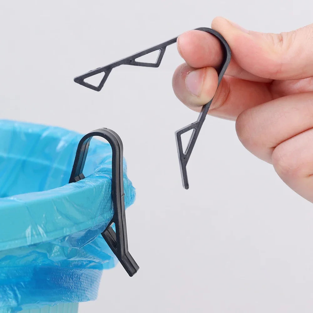 A hand holds black plastic clips designed to secure garbage bags or snack bags onto a trash can.