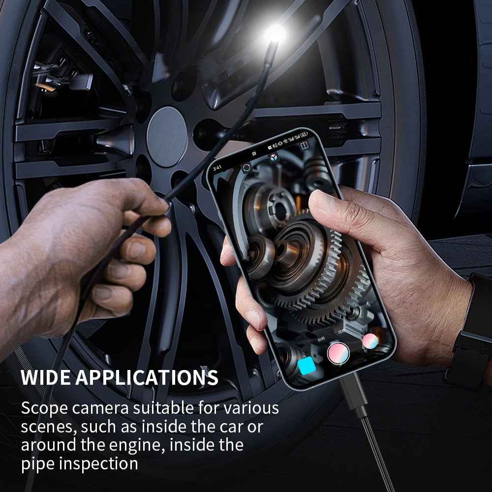 A hand holds a smartphone with an inspection camera connected to a cable, positioned near a car wheel for diagnostics.