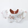 A white cotton baby feeding bib with a brown trim and a subtle floral pattern.