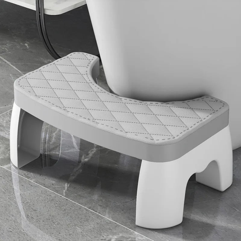 A white ergonomic non-slip toilet squat stool with a diamond-patterned seat is shown on a glossy floor.