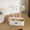 A white jewelry display rack with a drawer and wooden base holds various necklaces and earrings.