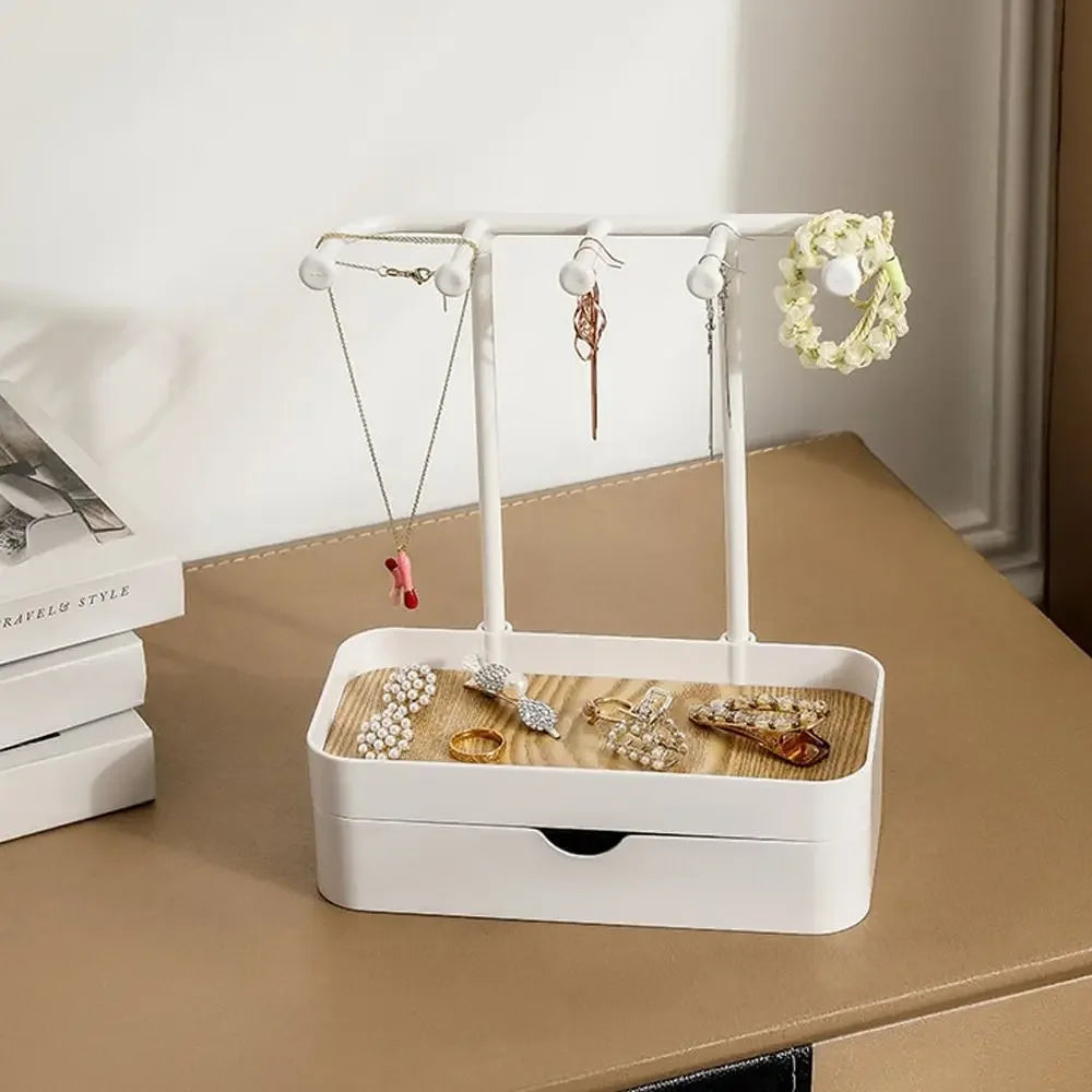 A white jewelry display rack with a drawer and wooden base holds various necklaces and earrings.