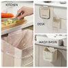 A set of foldable hanging trash cans in beige and pink are shown in kitchen, desk, and wash basin contexts.
