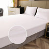 A white fitted mattress protector is shown on a bed, with a close-up view of the elastic edge.
